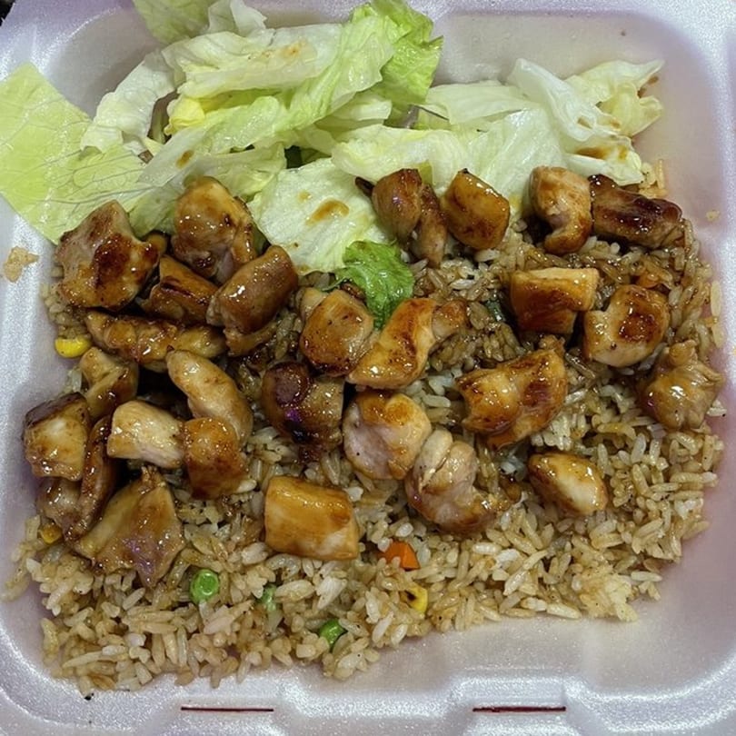 Teriyaki chicken and fried rice with a side of lettuce in a white takeout container.