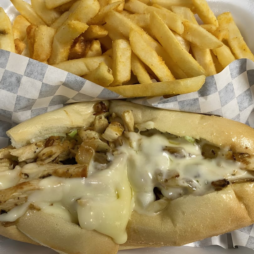 A chicken cheesesteak sandwich with melted cheese and onions, served with a side of golden fries.